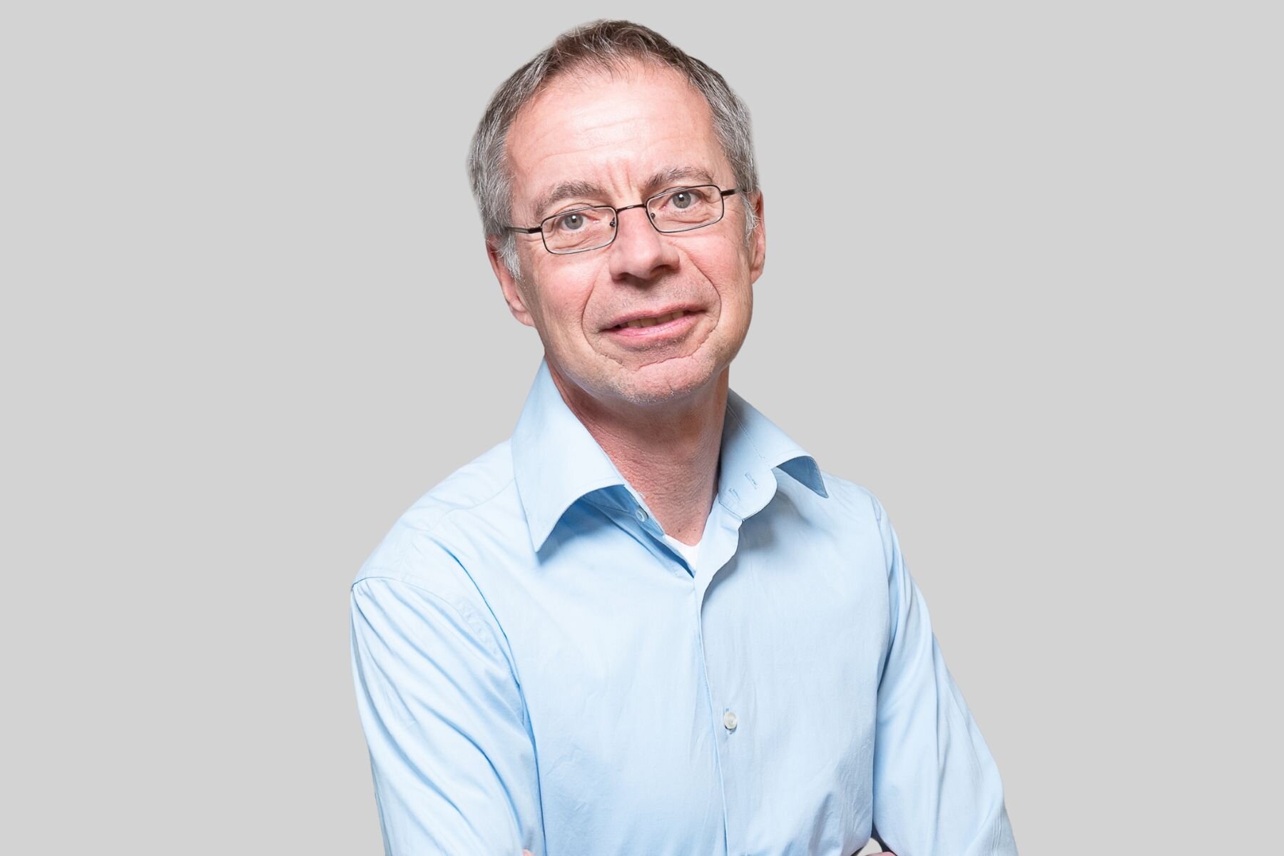 Mann mit Brille und blauem Hemd vor grauem Hintergrund.