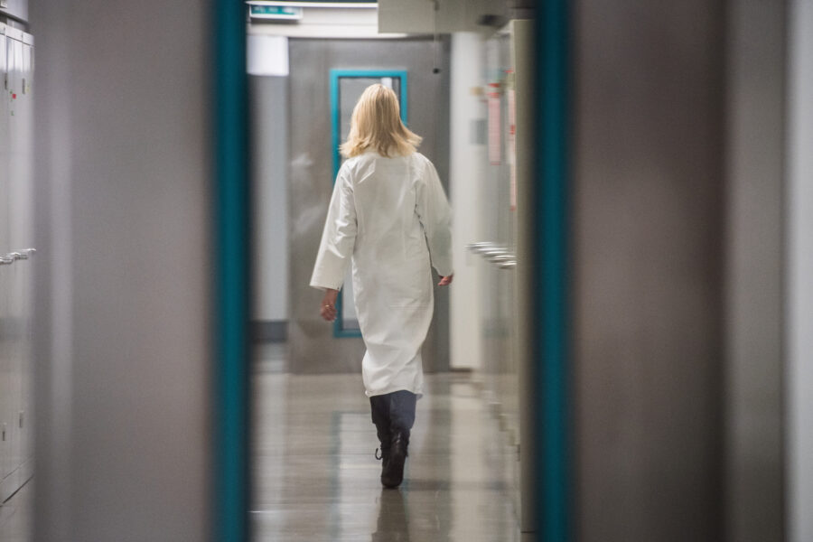 Person in weißem Kittel geht einen Flur entlang.