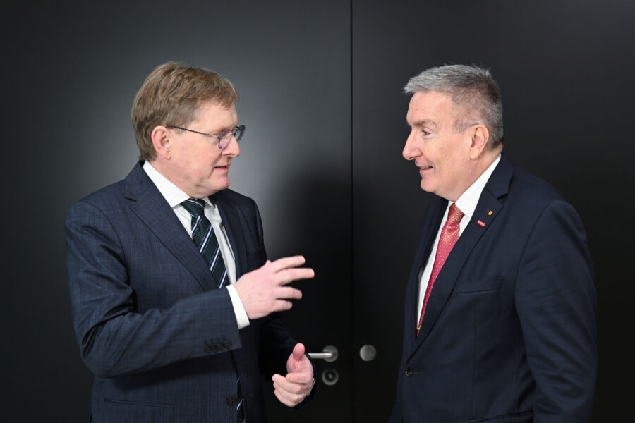 Zwei Männer im Anzug unterhalten sich vor einer schwarzen Tür.