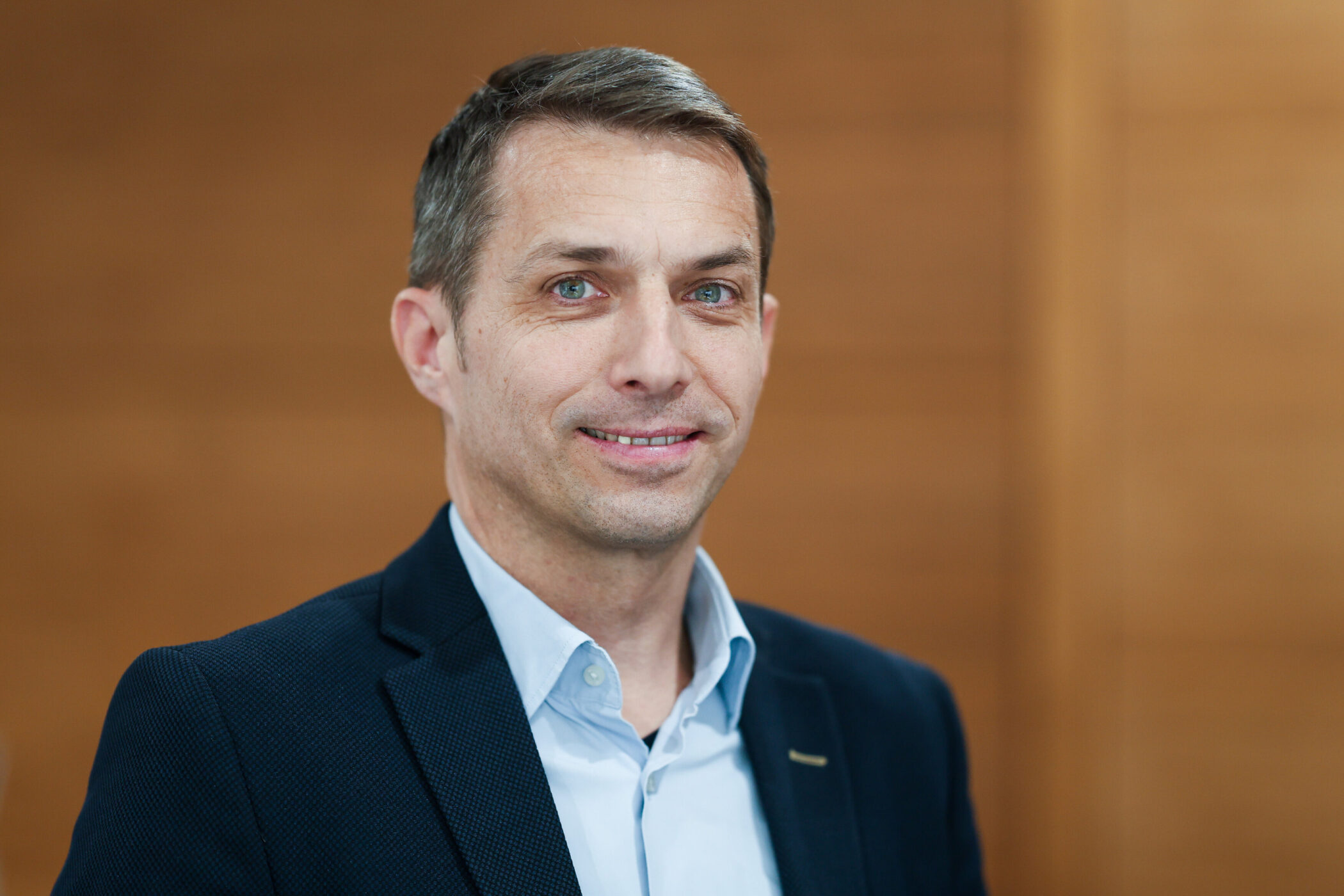 Mann in Anzug lächelt, Hintergrund unscharf.