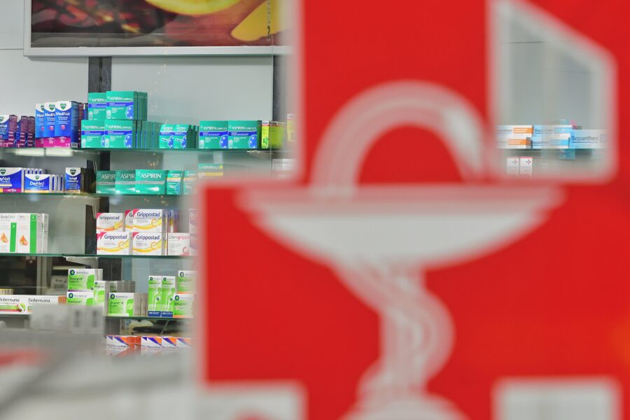 Rote Apotheken-Schlange im Vordergrund, Regale mit Medikamenten im Hintergrund.