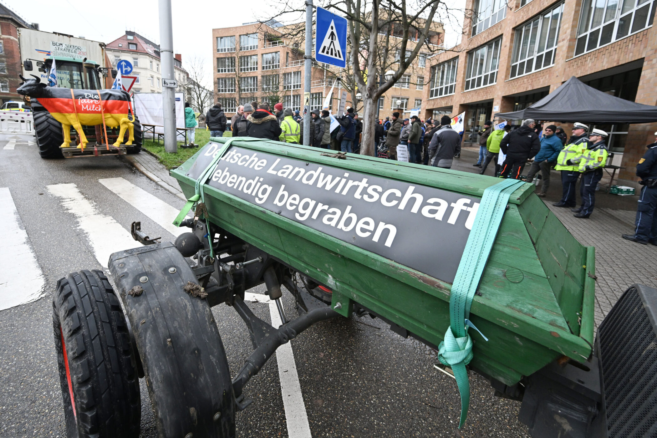 Grüner Sarg mit Aufschrift, Menschenmenge und Polizei im Hintergrund.