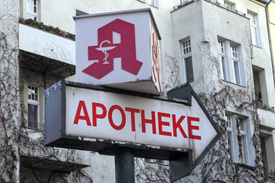 Apothekenschild mit rotem "A" und Schriftzug "APOTHEKE" auf einem Pfeil.