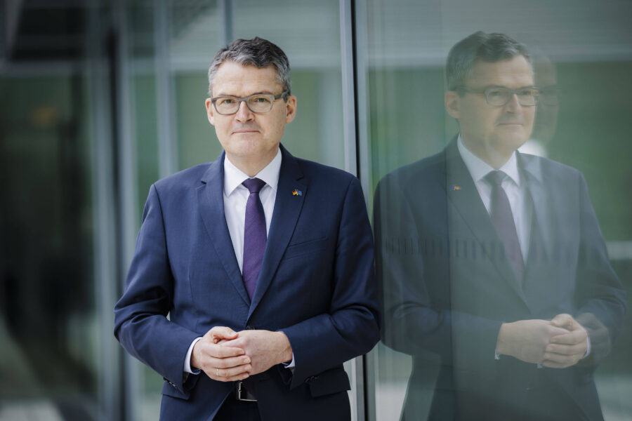 Mann im Anzug steht vor Glaswand, Spiegelbild sichtbar.