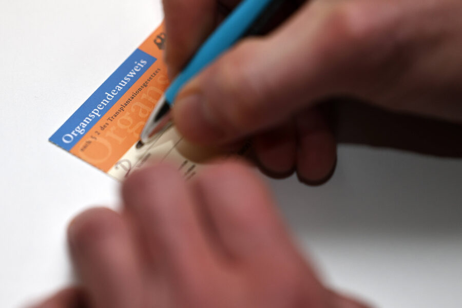 Hand schreibt auf einen Organspendeausweis mit blauem Stift.