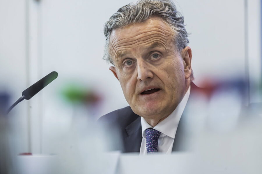 Älterer Mann spricht in ein Mikrofon, unscharfe Flaschen im Vordergrund.