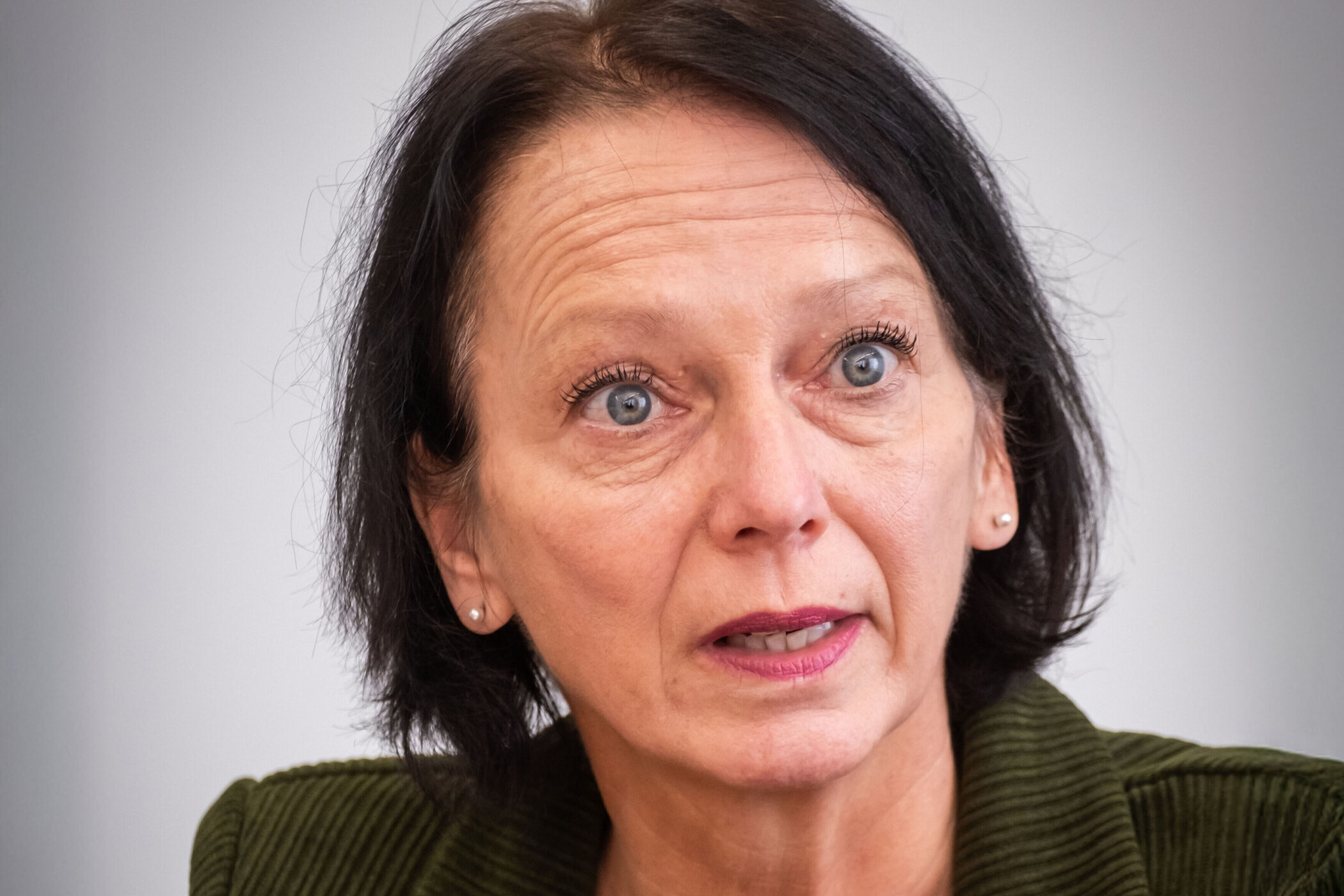 Eine Frau mit dunklem Haar und grünem Oberteil spricht.