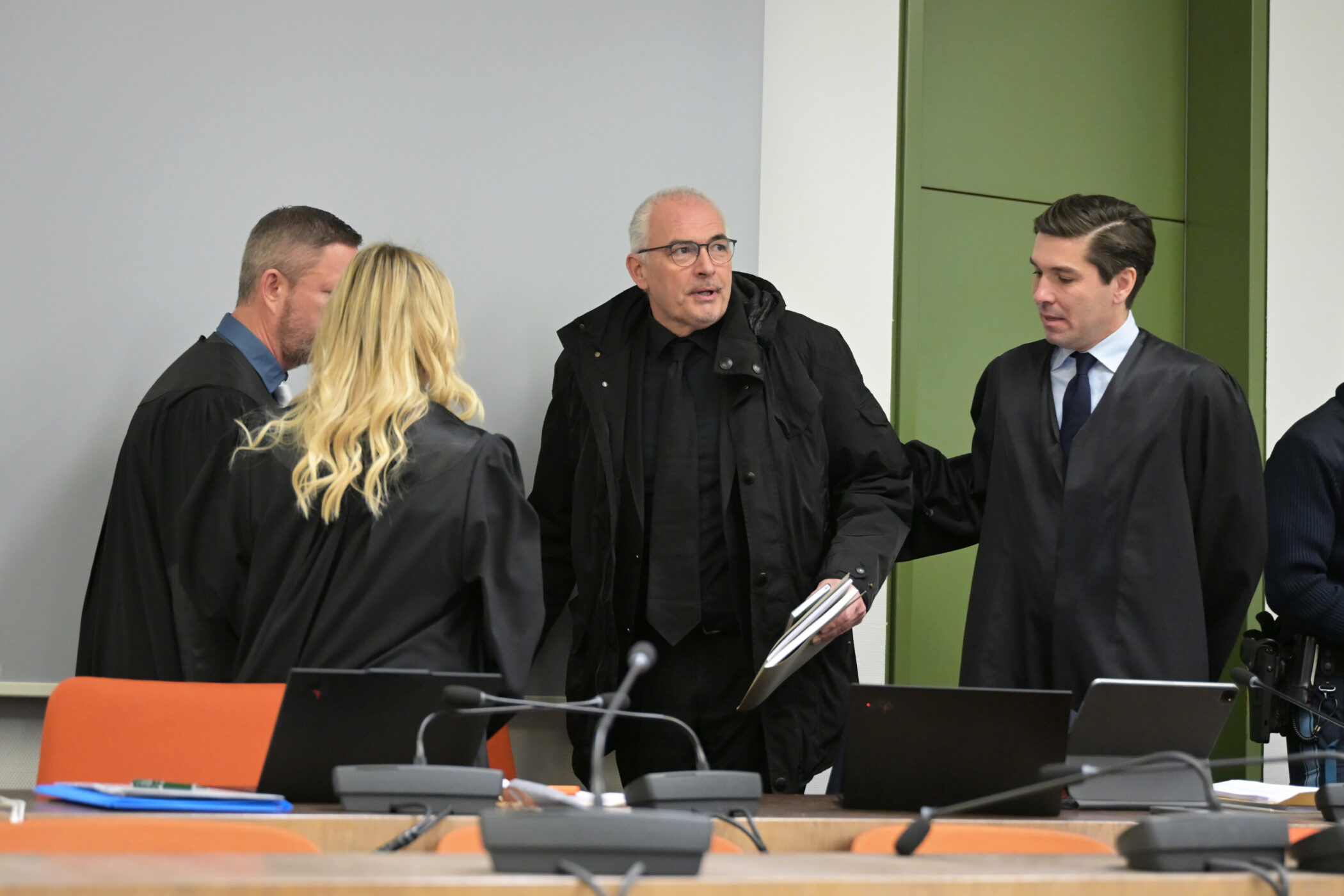 Fünf Personen in einem Raum, einige in Roben, sprechen miteinander.