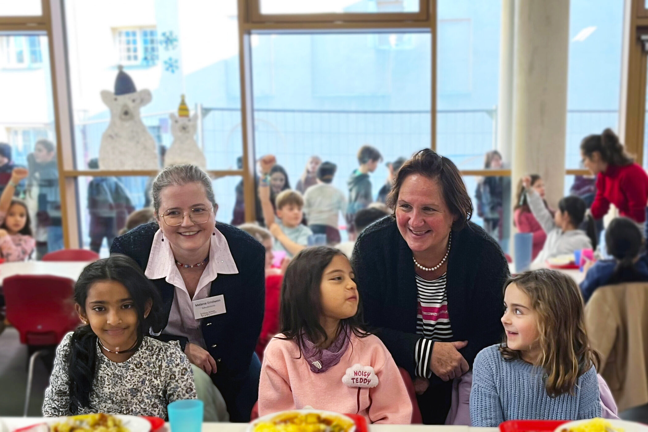 Zwei Erwachsene und drei Kinder sitzen an einem Tisch in einem belebten Raum.
