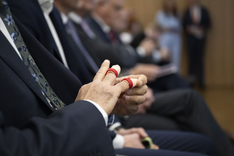 Person in Anzug mit Pflastern an zwei Fingern, im Hintergrund unscharfe Personen.