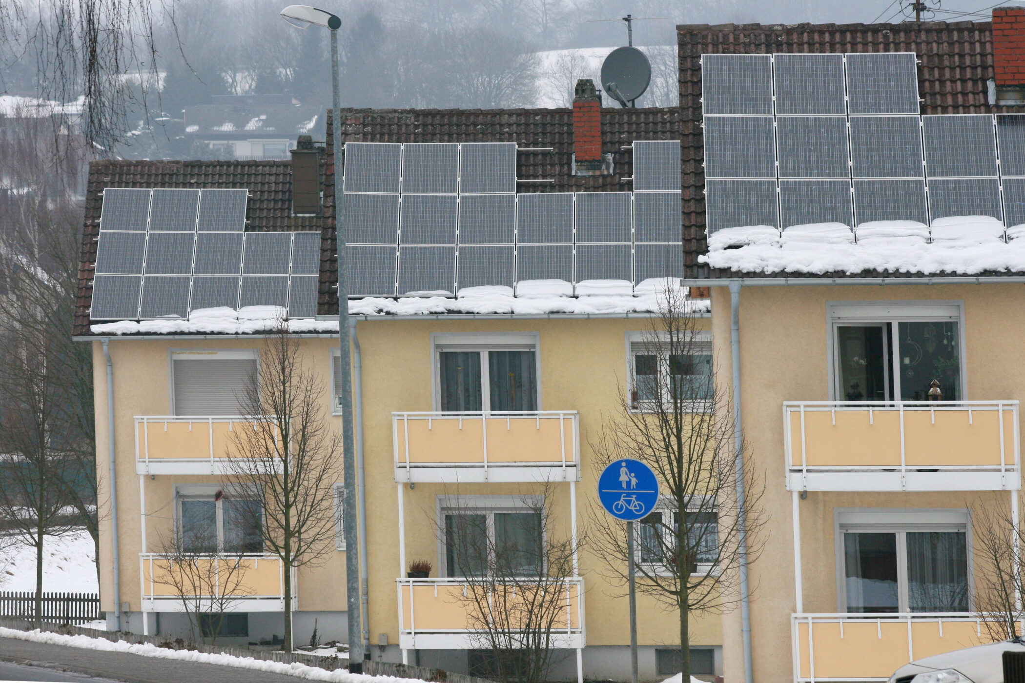 Mehrfamilienhaus mit Solarpanels, Schnee auf dem Dach, Verkehrsschild vorne.