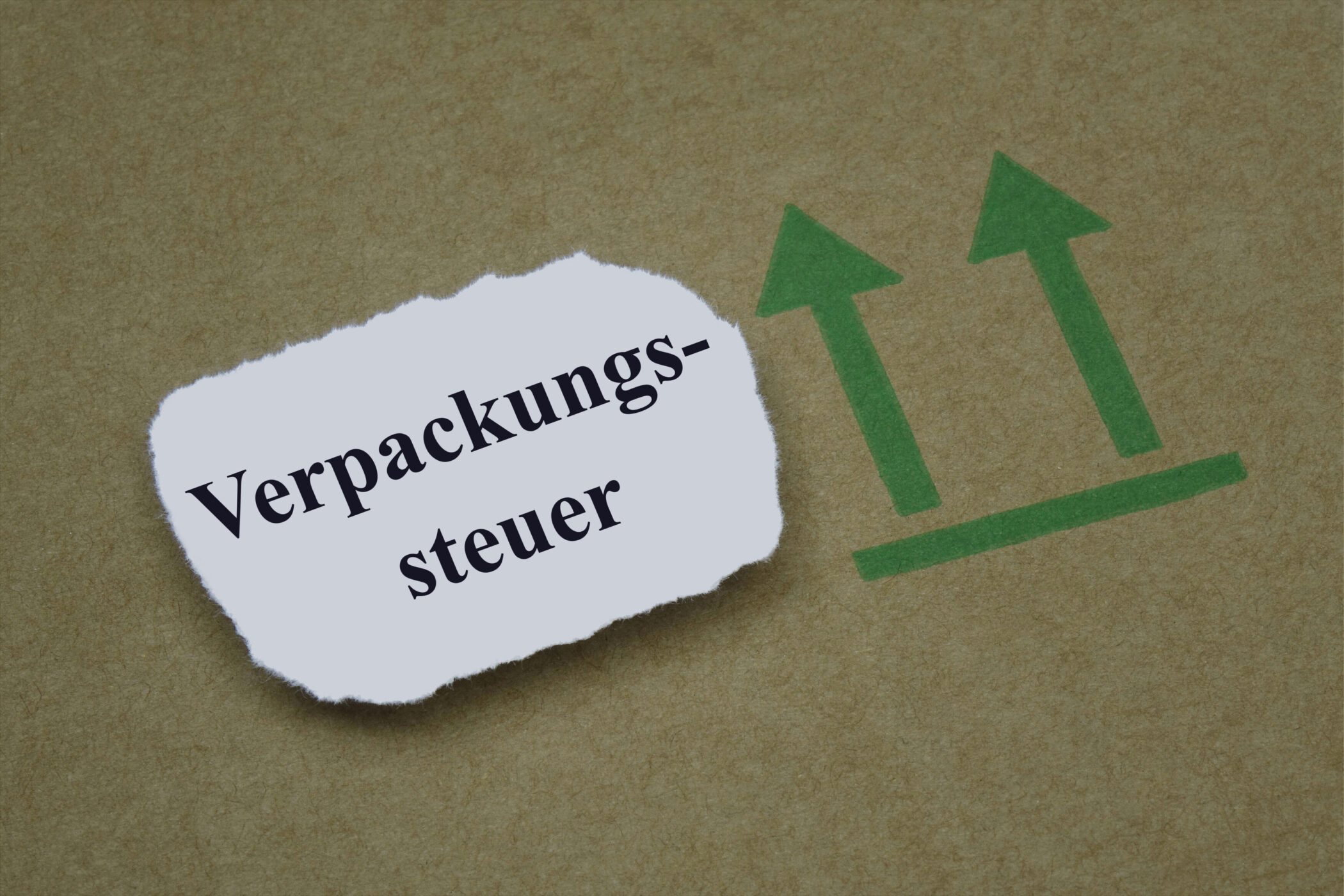 Zerrissenes Papier mit "Verpackungssteuer", daneben zwei grüne Pfeile nach oben.