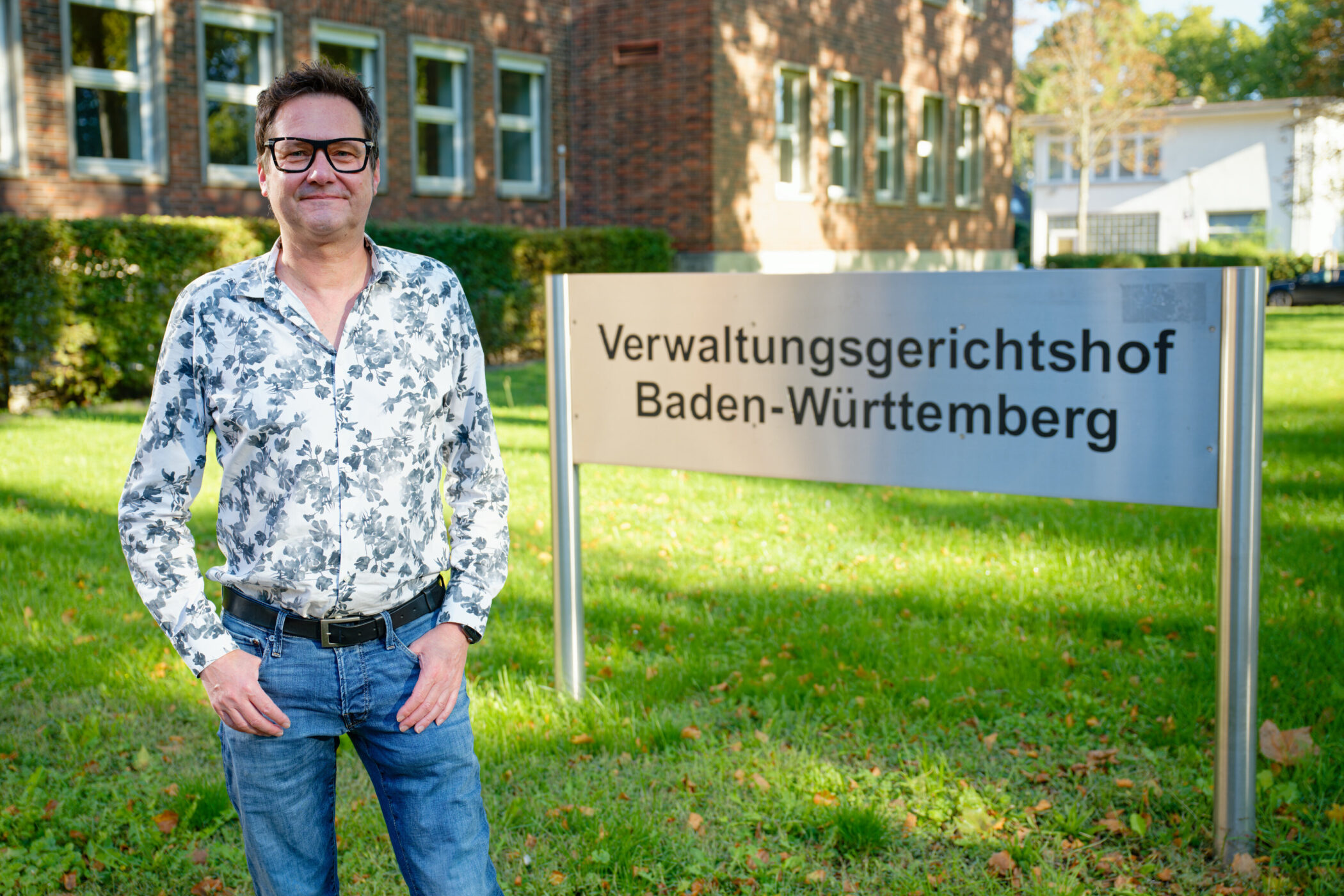 Person vor Schild "Verwaltungsgerichtshof Baden-Württemberg" auf Rasenfläche.