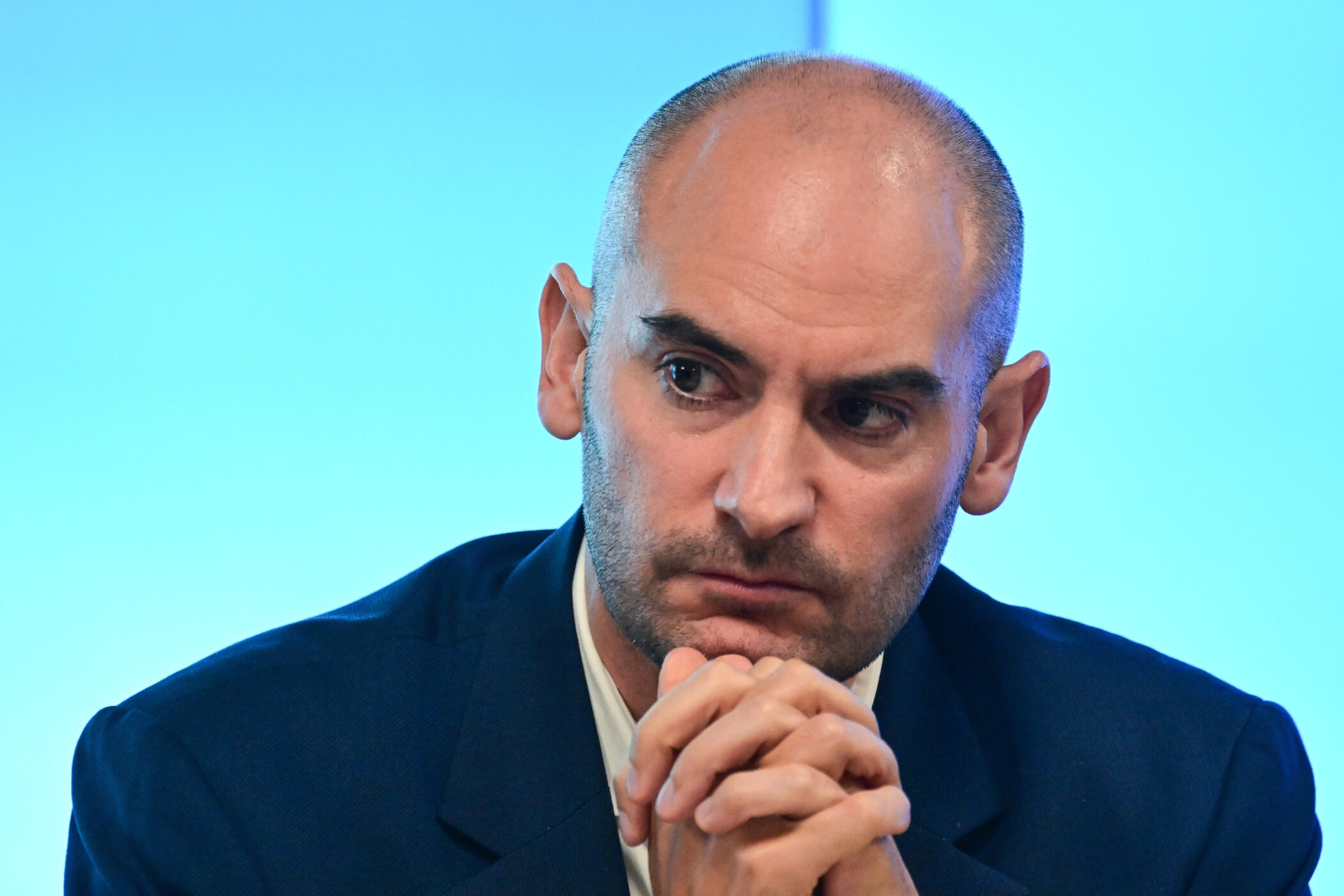 Ein Mann mit Glatze und Bart schaut zur Seite, Hände gefaltet.