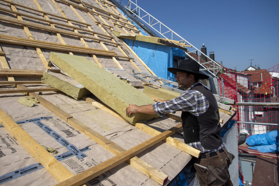 Arbeiter in Arbeitskleidung legt Dämmplatten auf ein Dach.