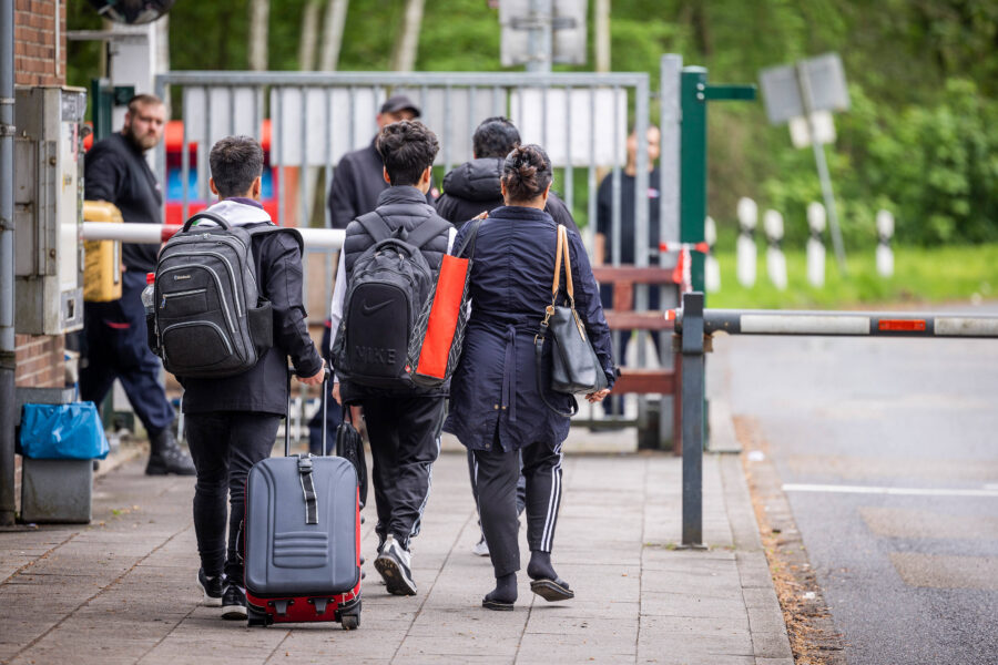 Vier Personen gehen mit Gepäck eine Straße entlang.