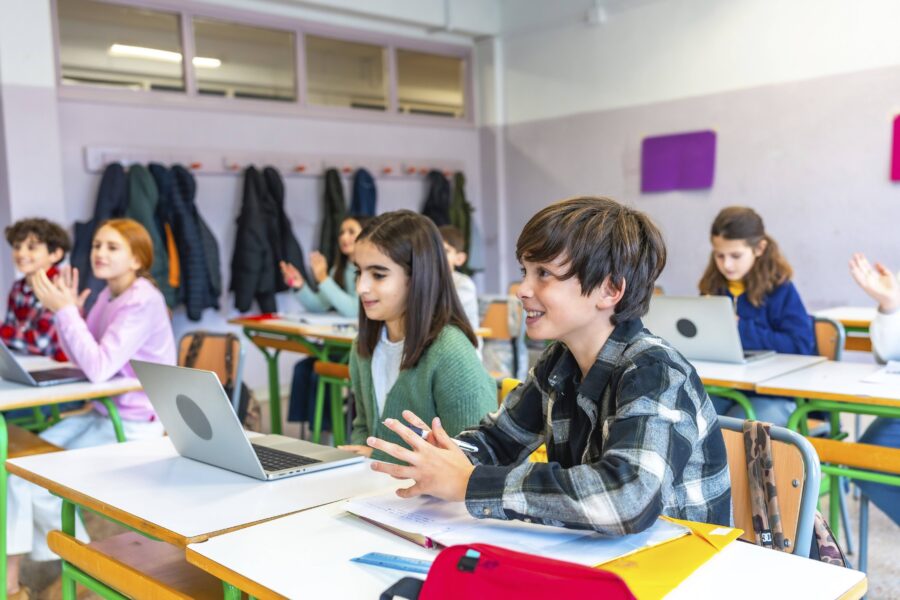 Mehrere Kinder sitzen in einem Klassenzimmer an Tischen mit Laptops.