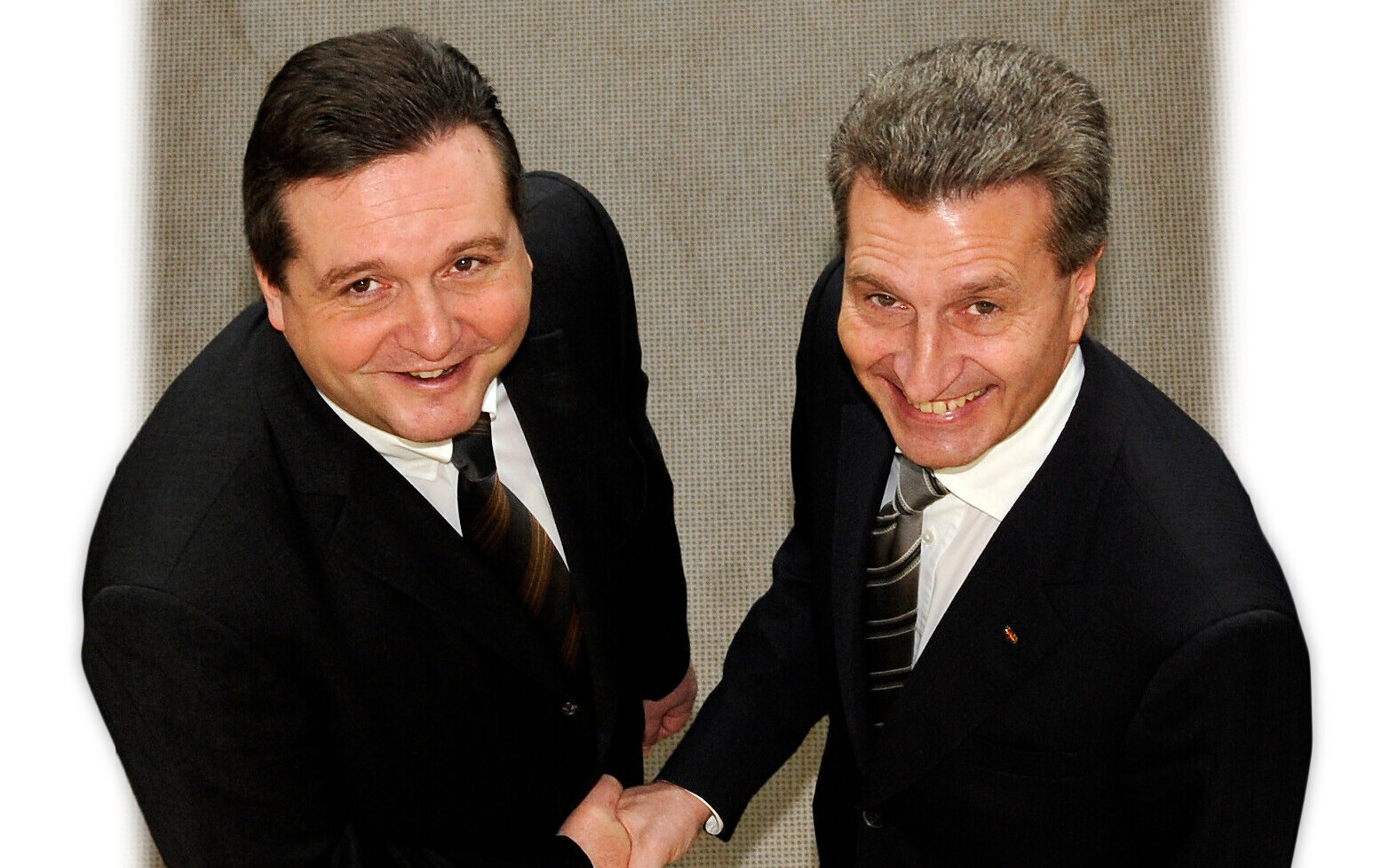 Zwei Männer in Anzügen schütteln sich die Hand und lächeln in die Kamera.