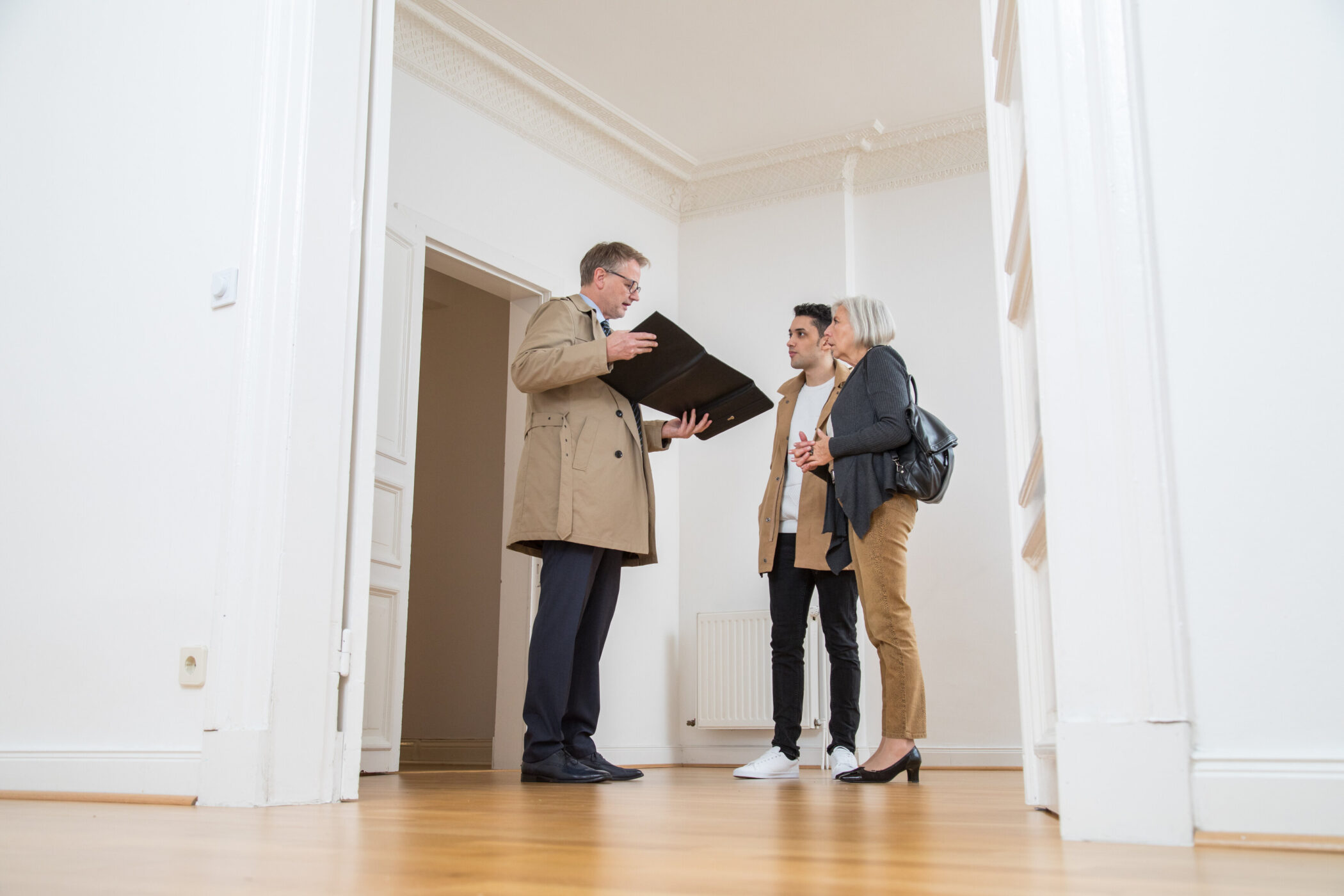 Drei Personen in einem leeren Raum, eine Person hält eine Mappe.