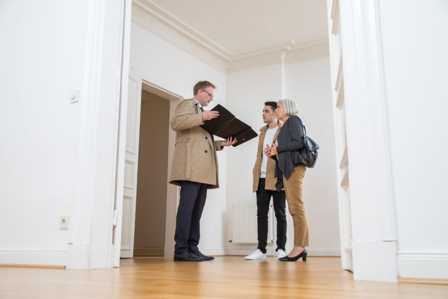 Drei Personen in einem leeren Raum, eine Person hält eine Mappe.