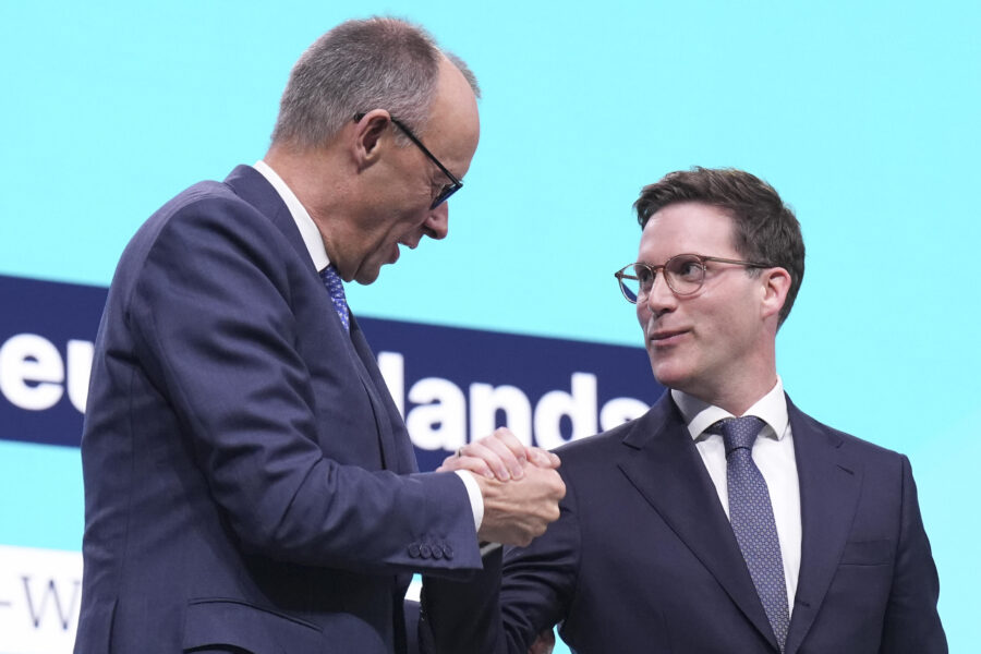 Zwei Männer in Anzügen und Brillen geben sich die Hand.