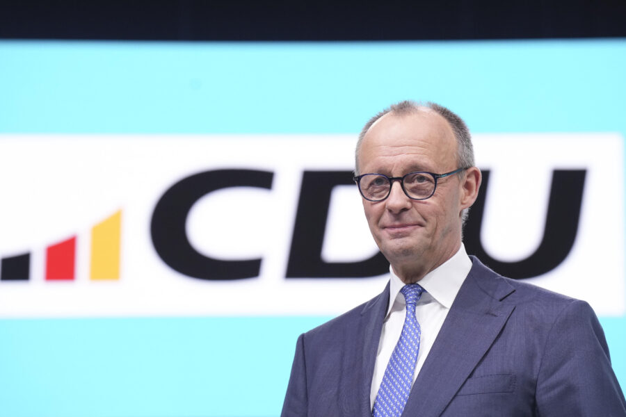 Ein Mann im Anzug steht vor einem CDU-Logo auf einem hellblauen Hintergrund.