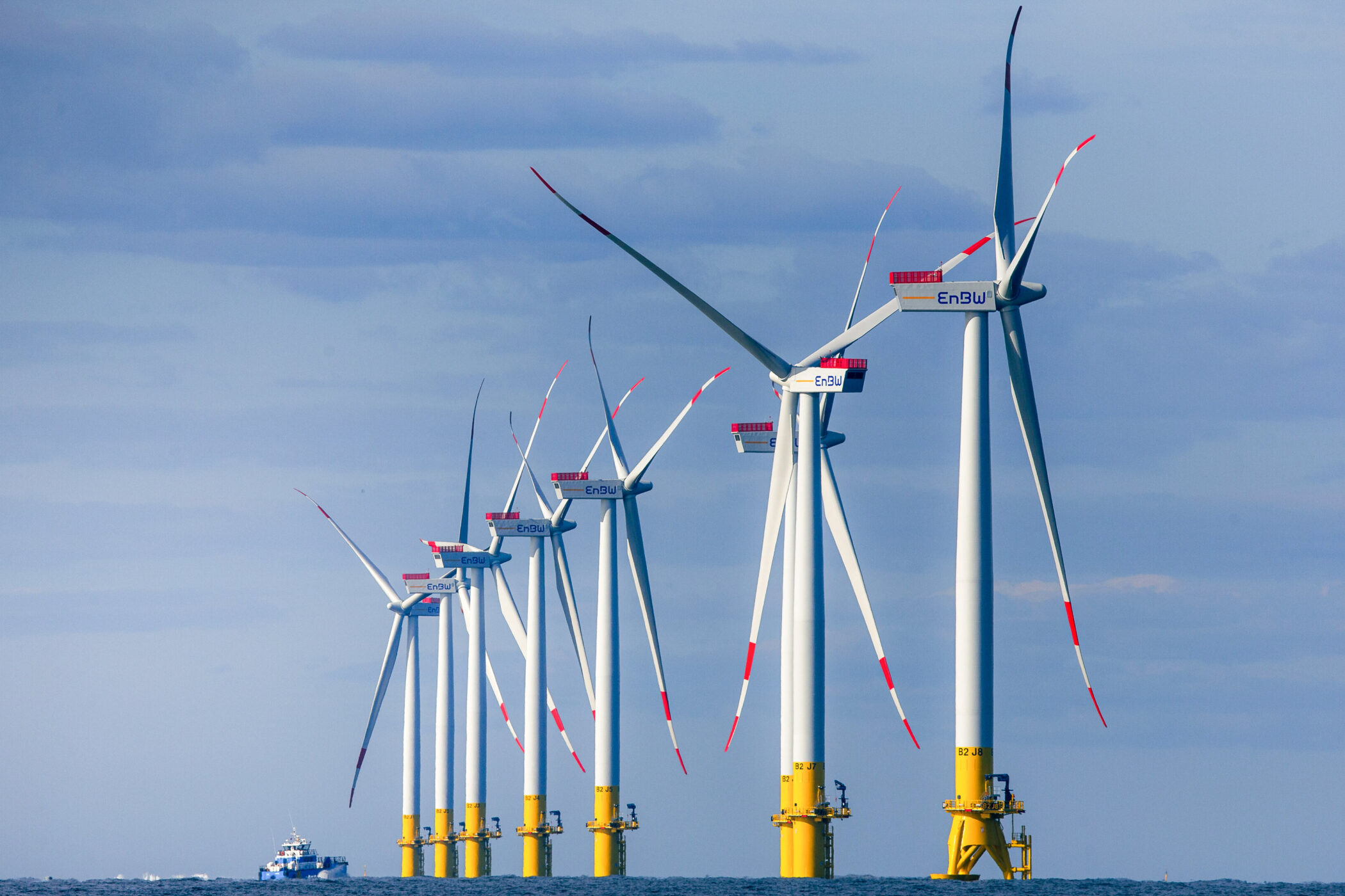 Reihe von Windkraftanlagen im Meer, kleines Boot im Hintergrund.