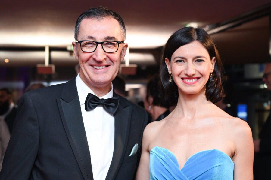 Ein Mann im Anzug und eine Frau im blauen Kleid lächeln in die Kamera.