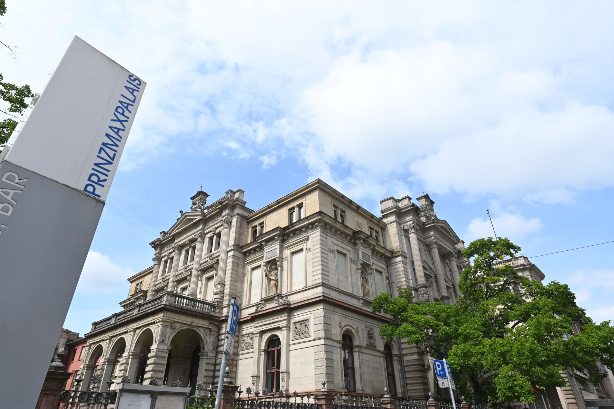 Historisches Gebäude mit Säulen, Baum rechts, Schild "PRINZMAXPALIAS" links.
