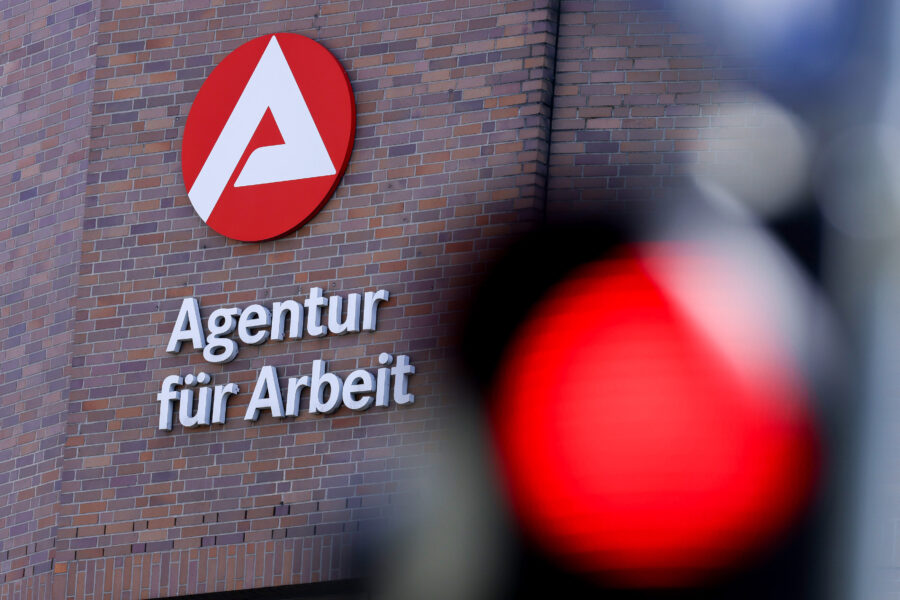 Logo der Agentur für Arbeit auf Backsteinwand, unscharfes rotes Licht im Vordergrund.