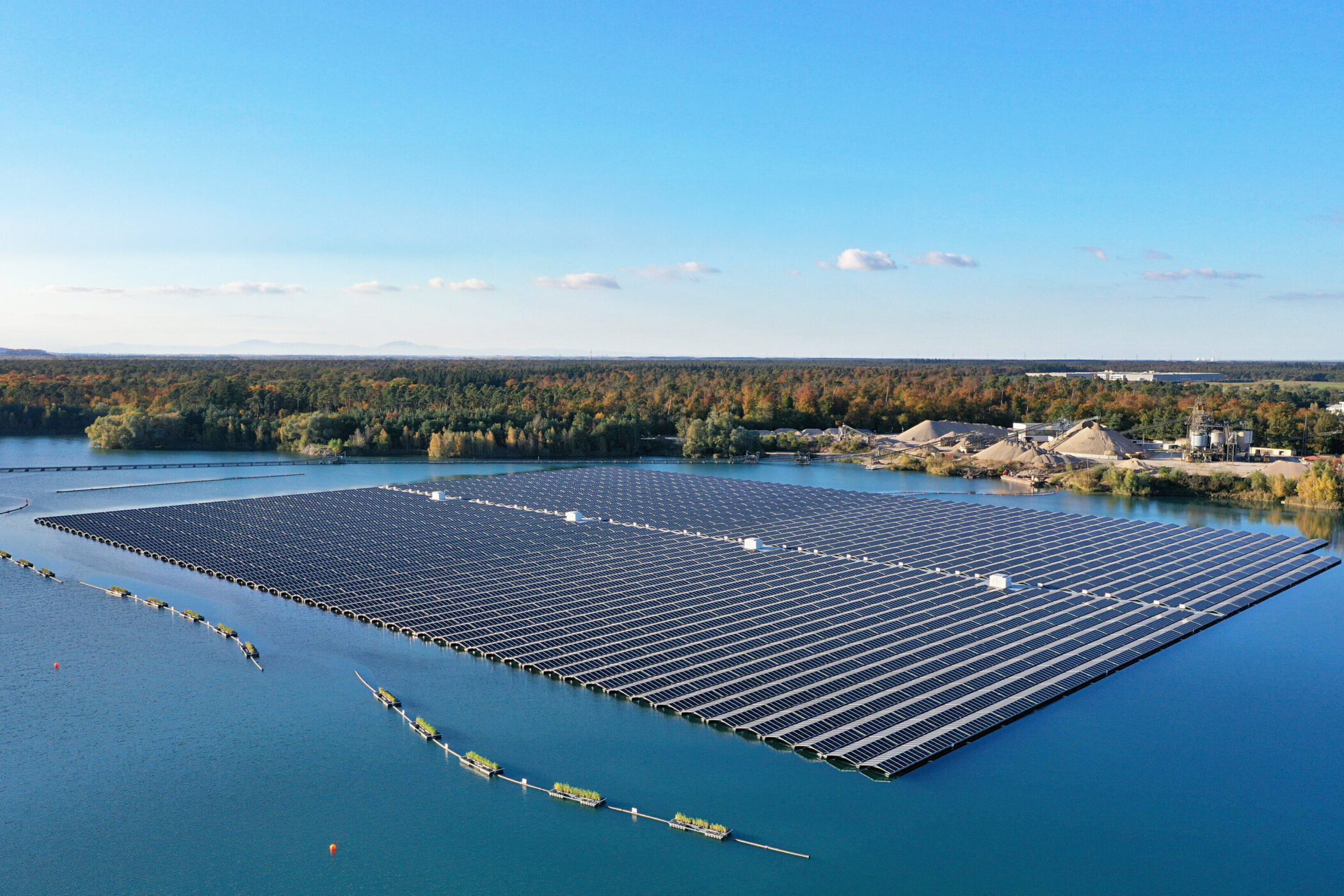 Schwimmende Solaranlage auf einem Gewässer, umgeben von Wald und Industrieanlagen.
