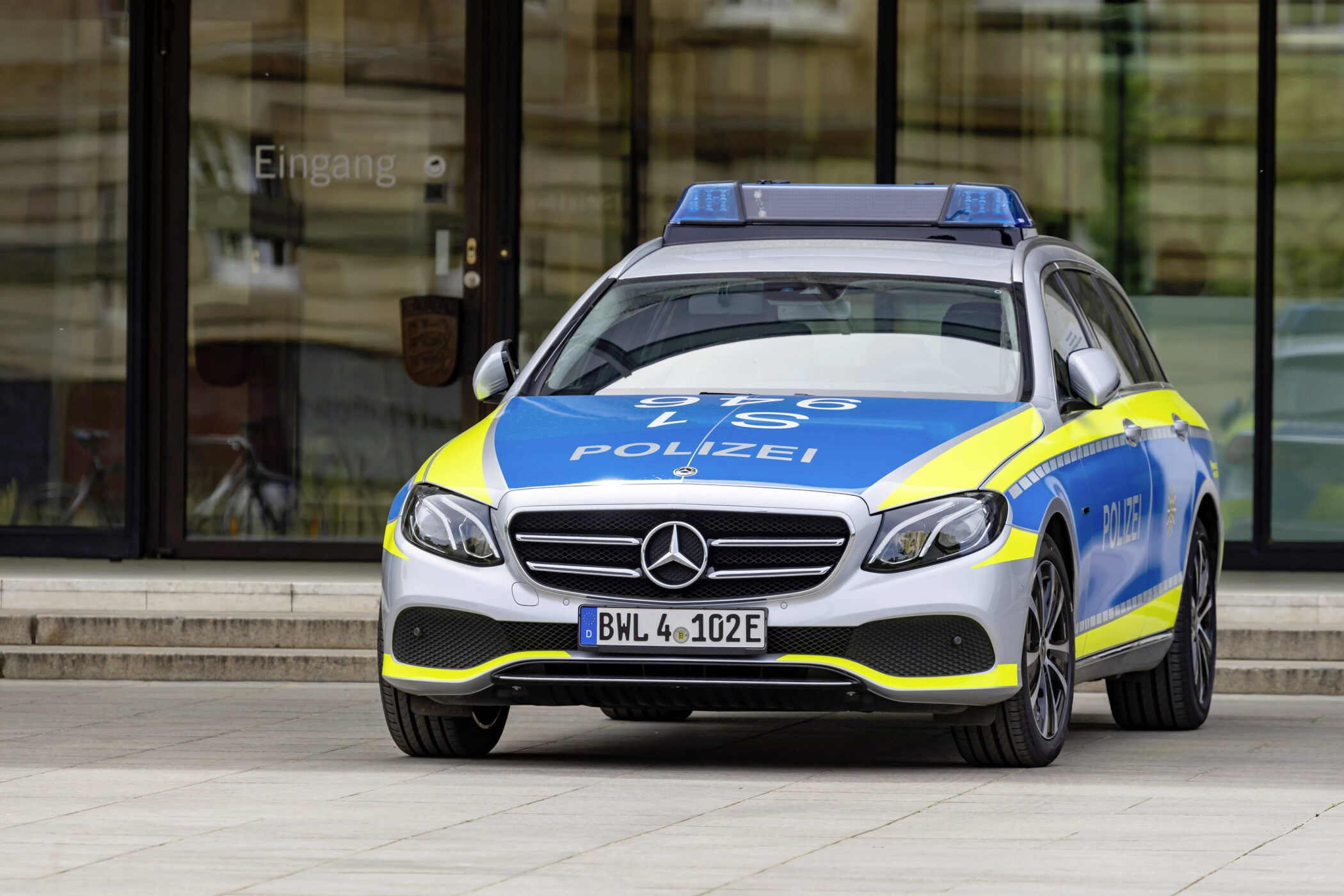 Silber-blaues Polizeiauto vor einem Gebäude mit der Aufschrift „Eingang“.