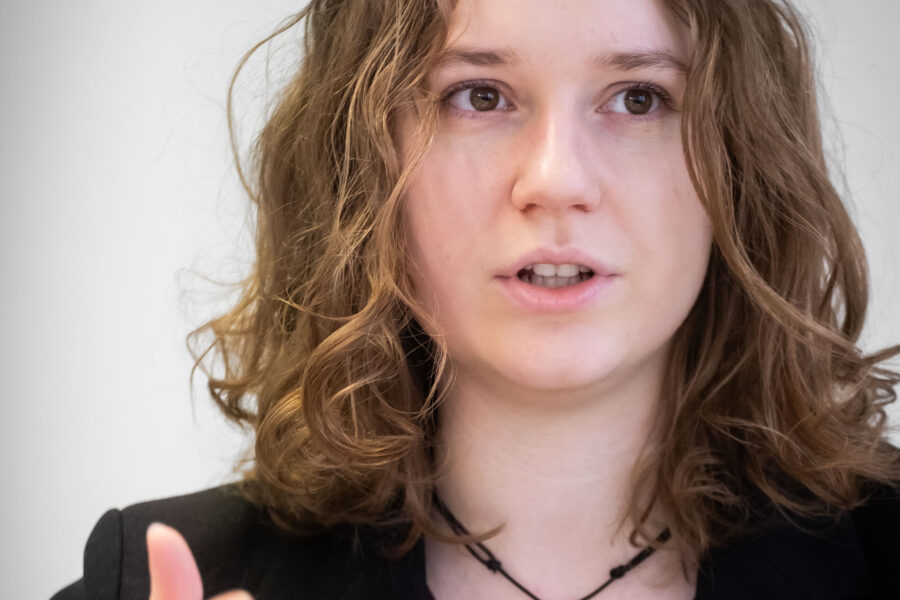 Eine Person mit lockigem Haar spricht, trägt eine Halskette.