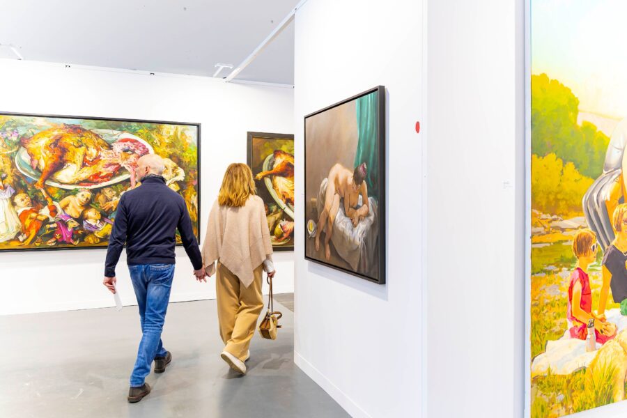 Zwei Personen gehen durch eine Kunstgalerie mit Gemälden an den Wänden.