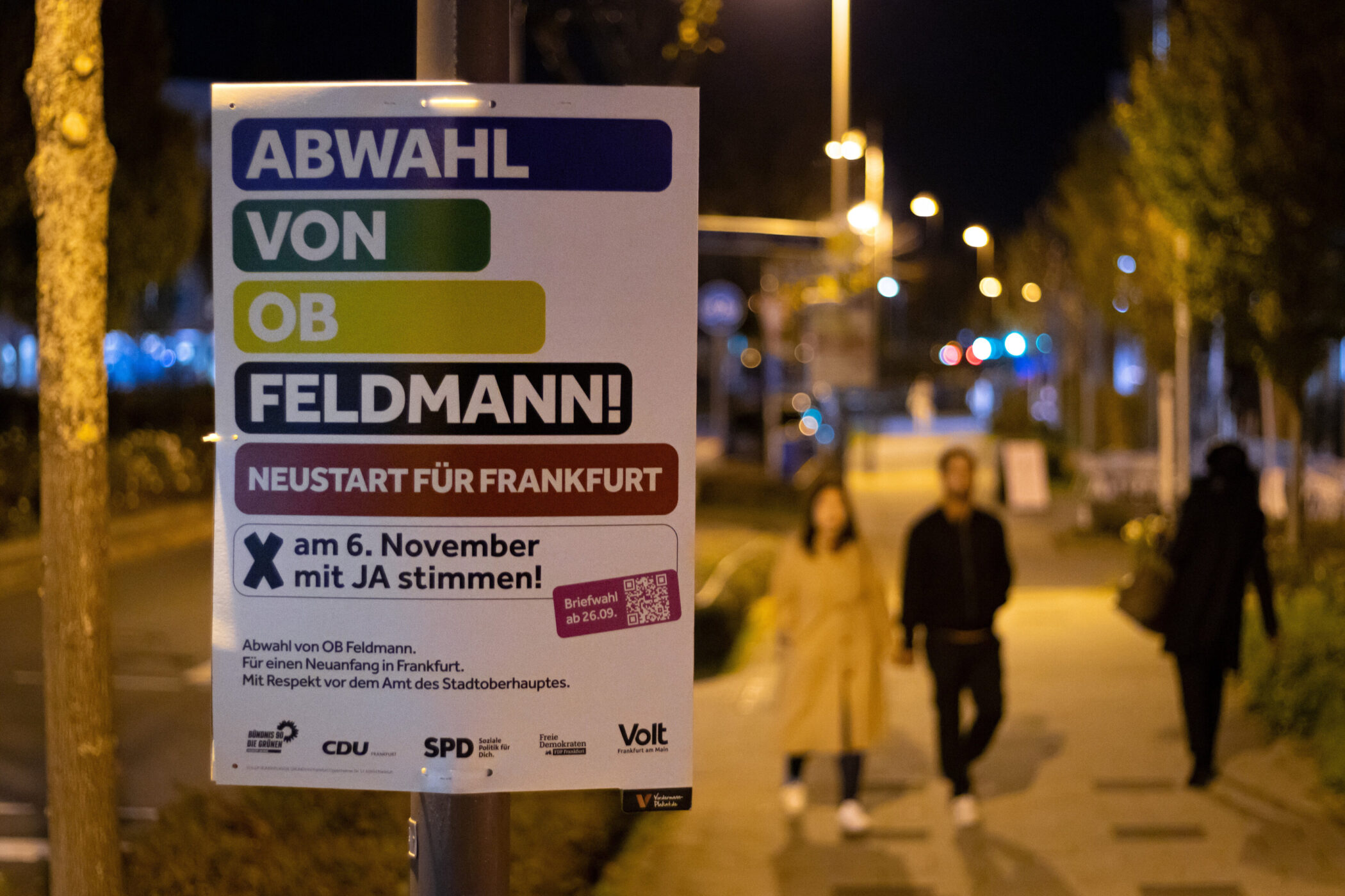 Plakat mit Text "Abwahl von OB Feldmann" an einer Straße bei Nacht.