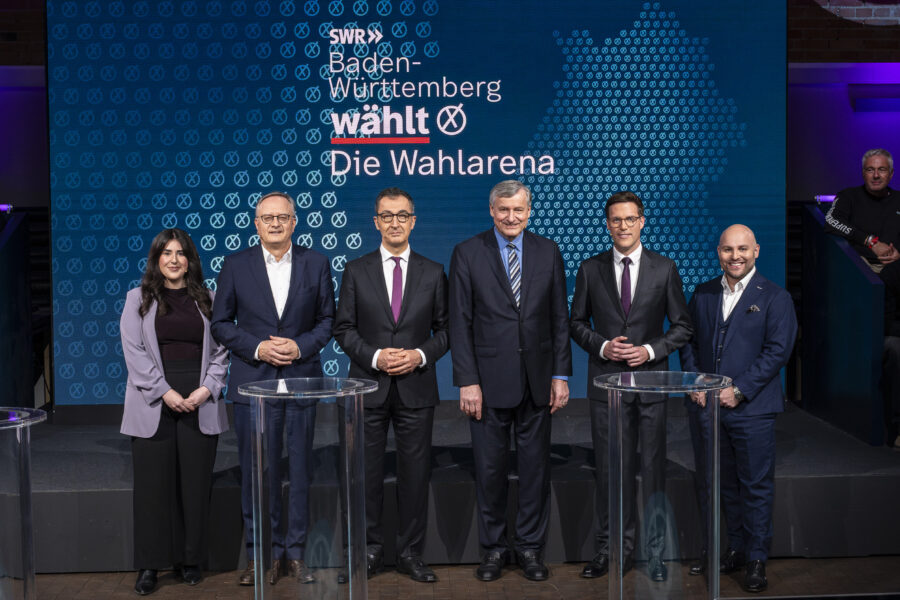Sechs Personen stehen vor einem Bildschirm mit "Baden-Württemberg wählt - Die Wahlarena".