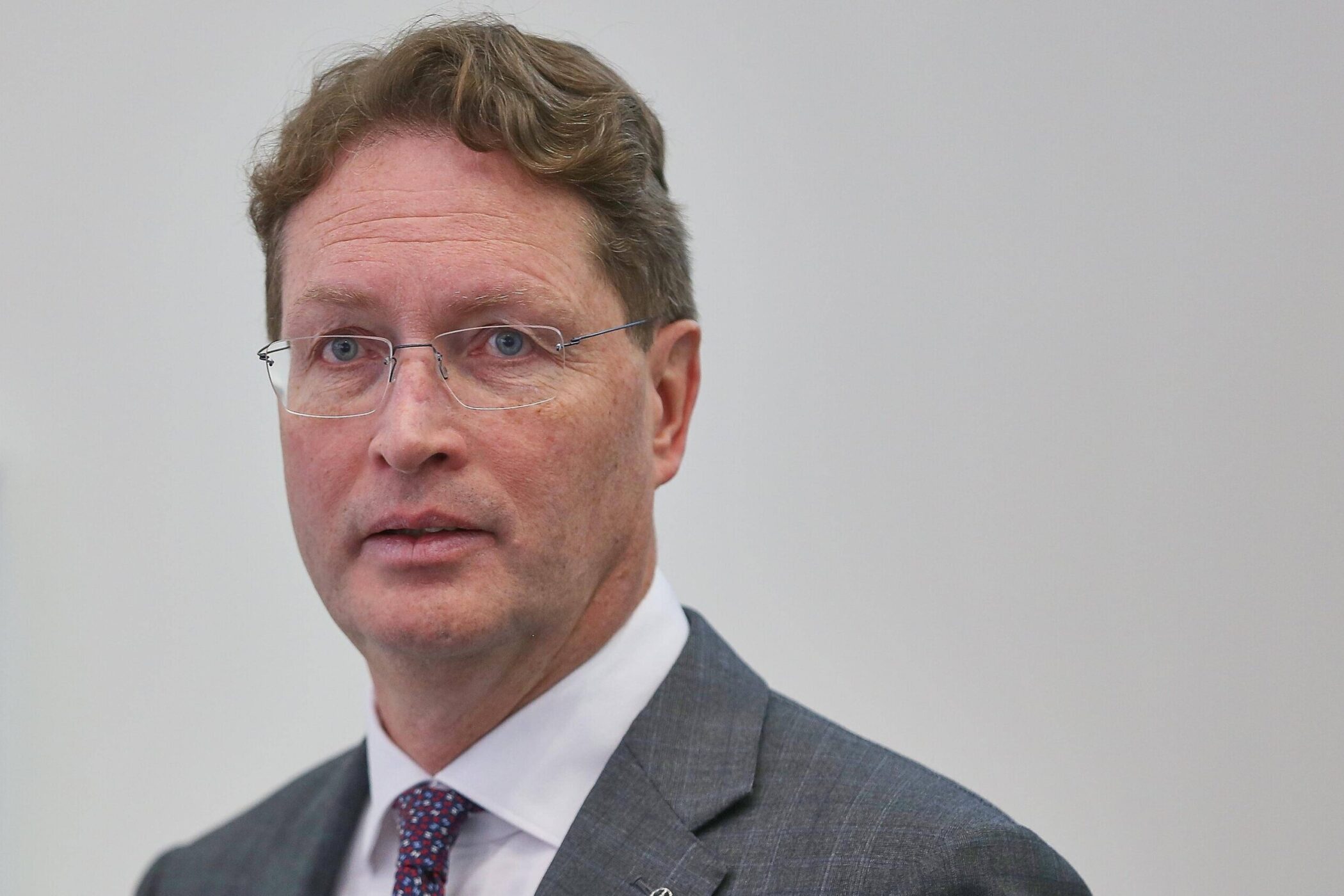 Ein Mann mit Brille und Anzug vor neutralem Hintergrund.