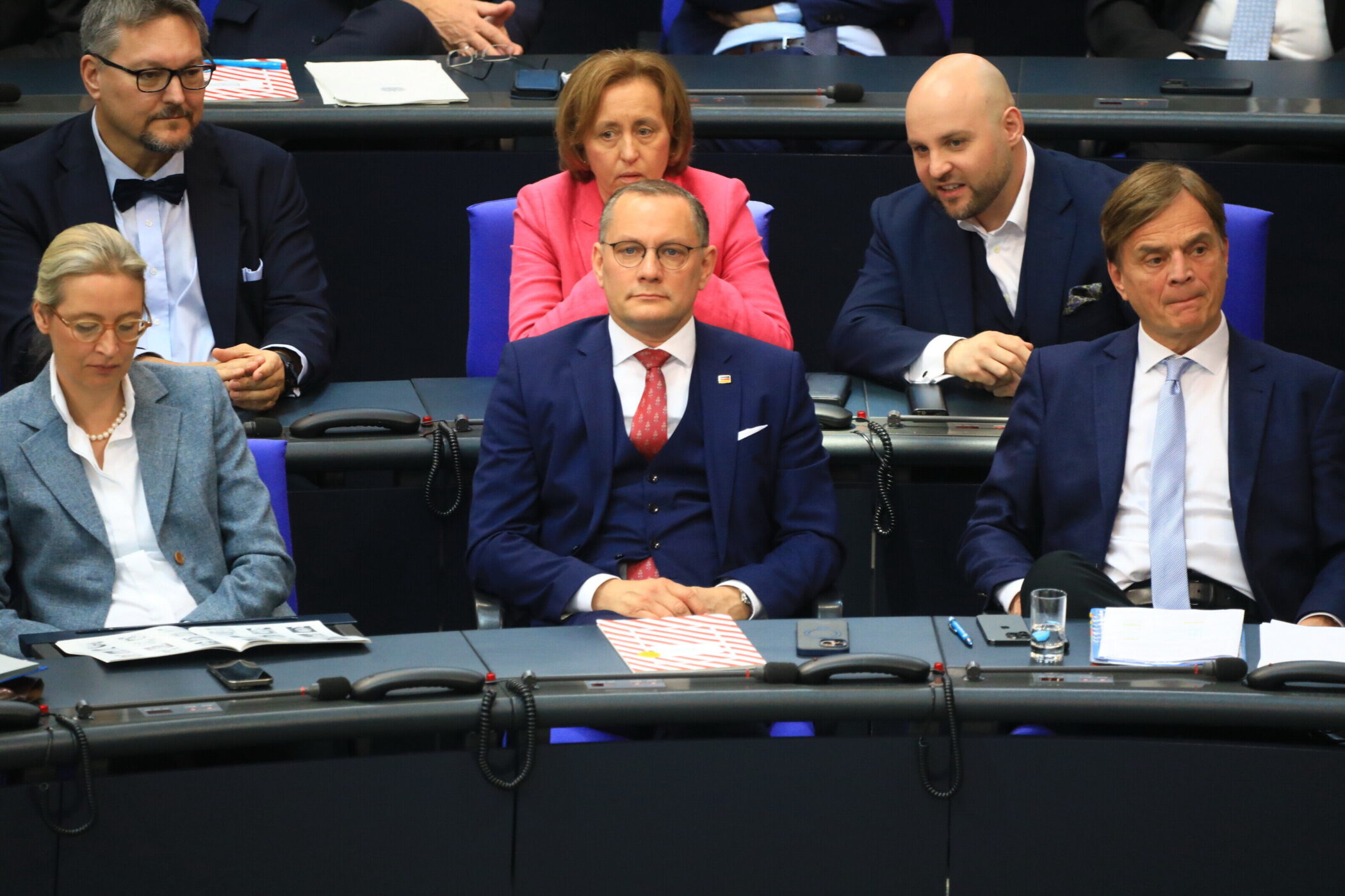 Sechs Personen in Anzügen sitzen in einer Reihe im Publikum.