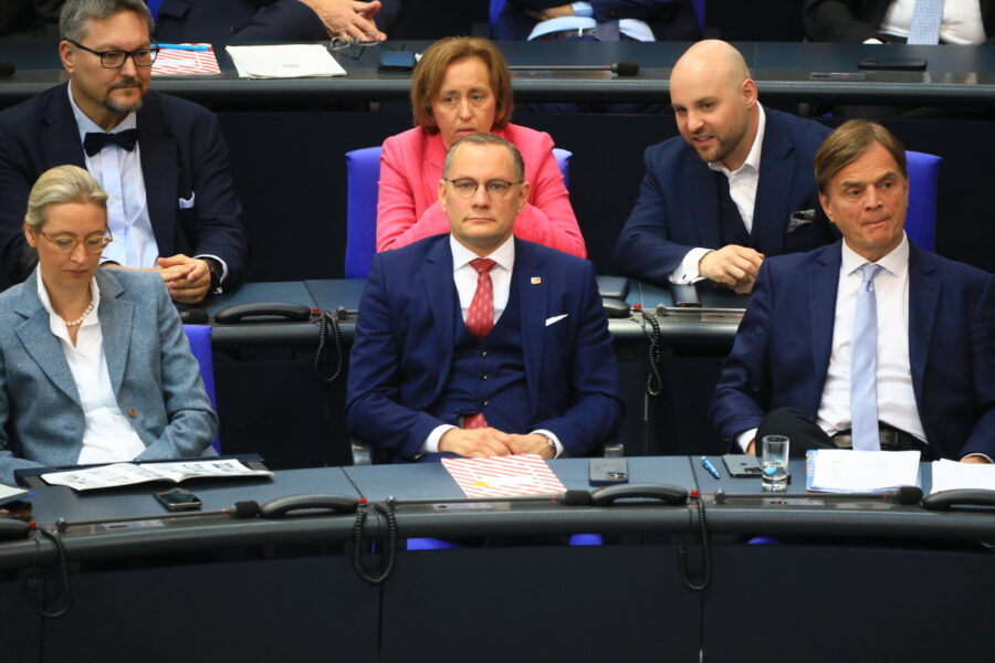 Sechs Personen in Anzügen sitzen in einer Reihe im Publikum.