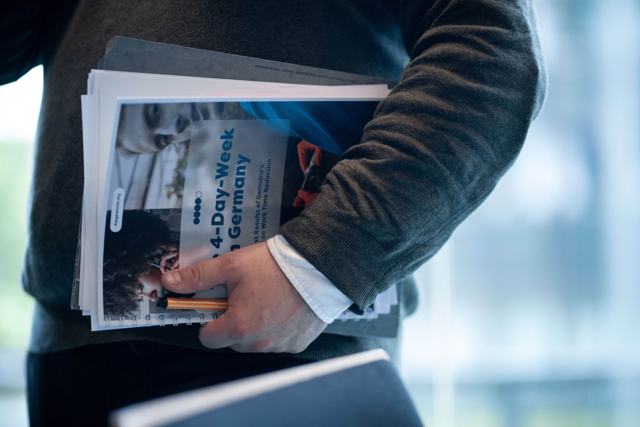 Person hält einen Stapel Unterlagen mit einem Deckblatt zur 4-Tage-Woche in Deutschland.