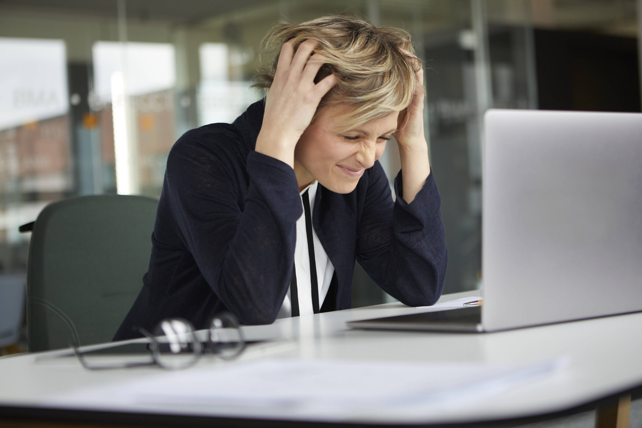 Person am Schreibtisch hält sich den Kopf, vor einem Laptop.