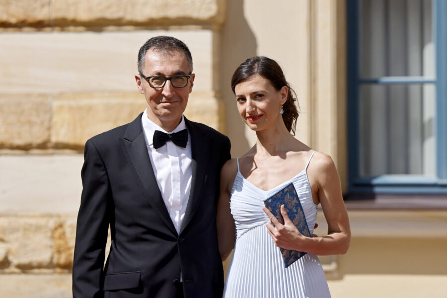 Ein Mann im Anzug und eine Frau im Kleid posieren vor einer Steinwand.