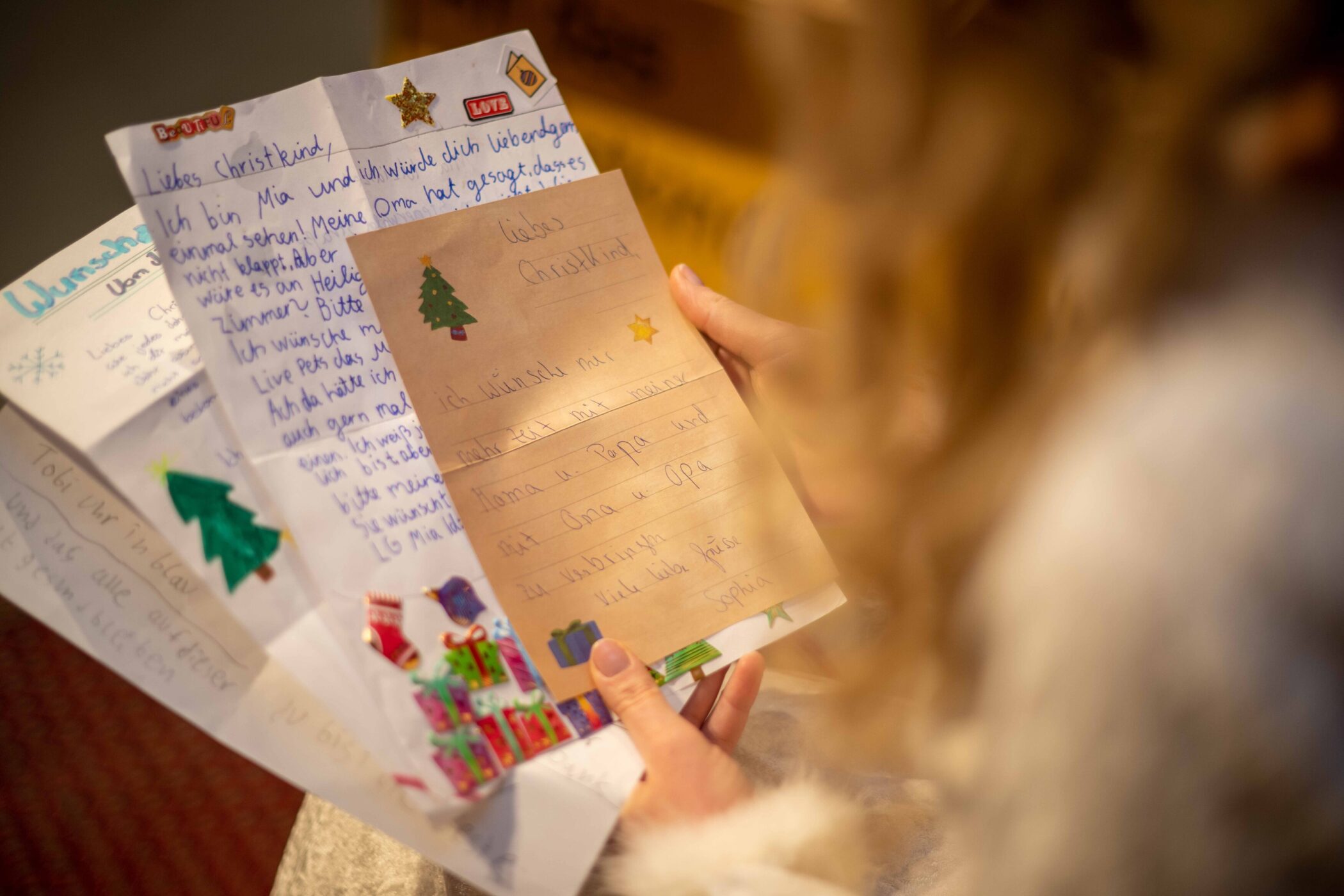 Person hält mehrere bunte Briefe mit weihnachtlichen Motiven und Aufklebern.