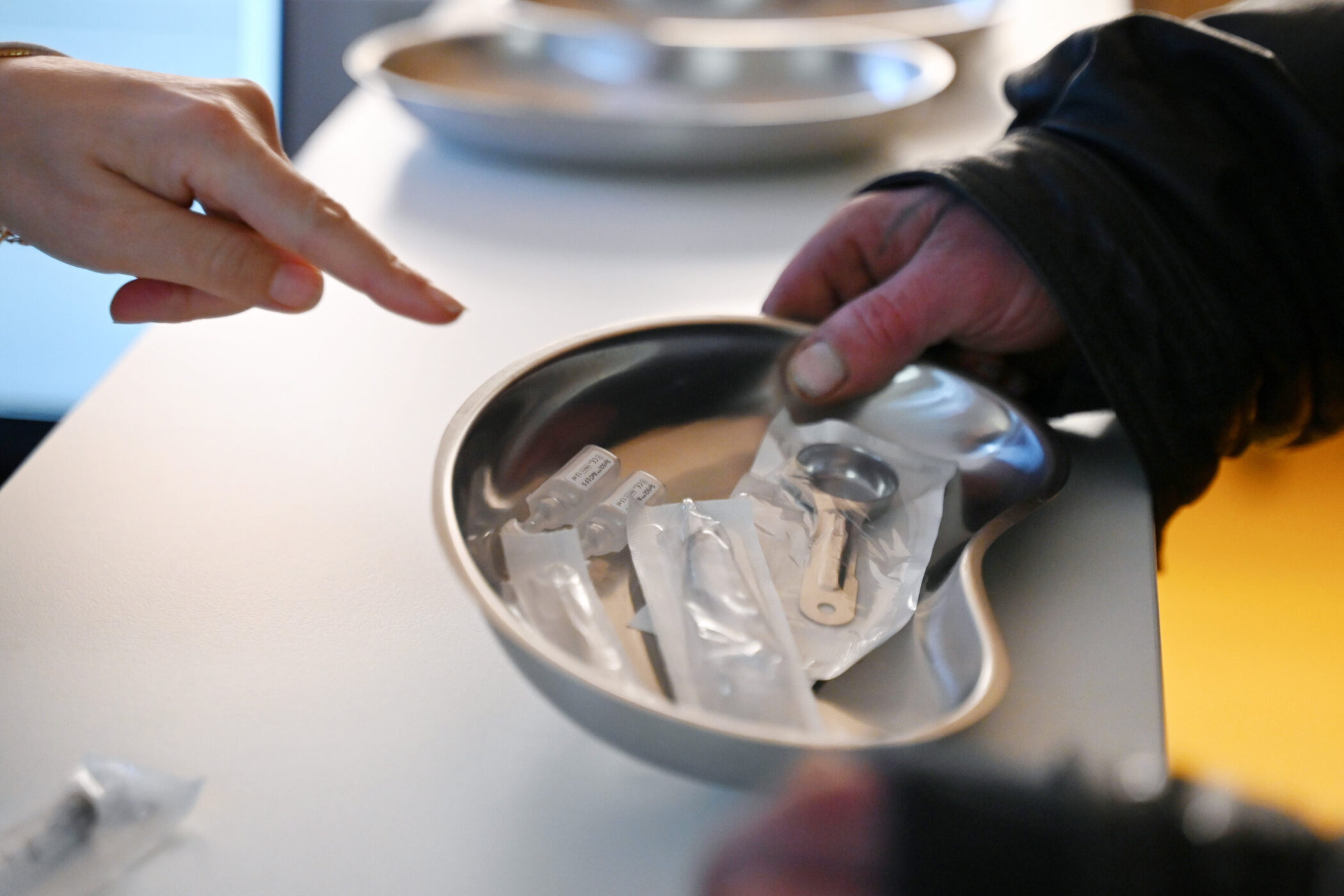 Zwei Hände, eine hält eine Nierenschale mit medizinischen Utensilien.