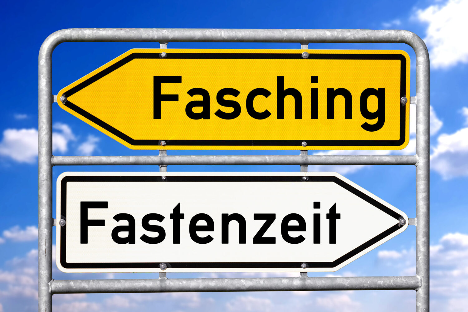 Gelbes Schild mit "Fasching", weißes Schild mit "Fastenzeit". Himmel im Hintergrund.