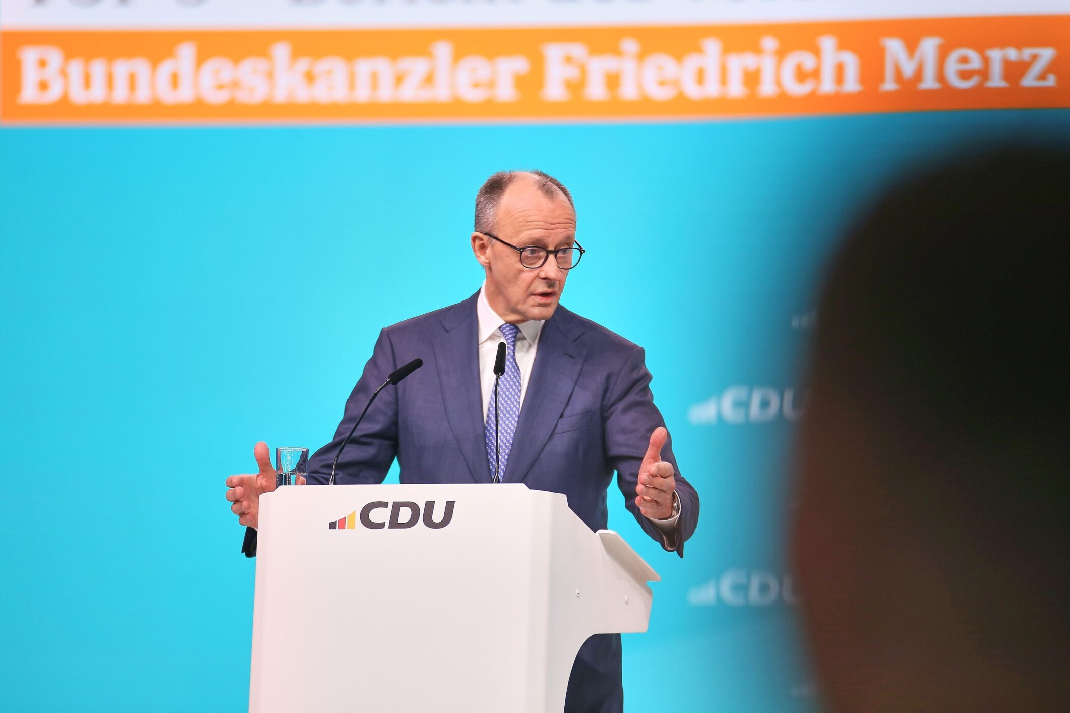 Ein Mann am Rednerpult, Hintergrund mit Schriftzug "Bundeskanzler Friedrich Merz".