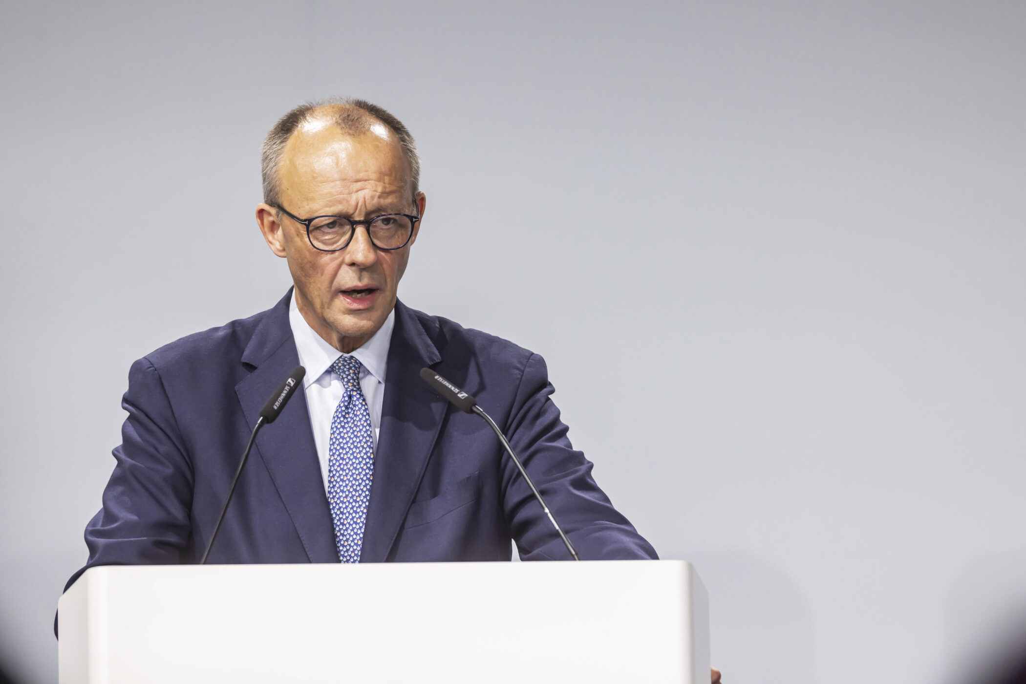 Ein Mann am Rednerpult, zwei Mikrofone, formelle Kleidung.