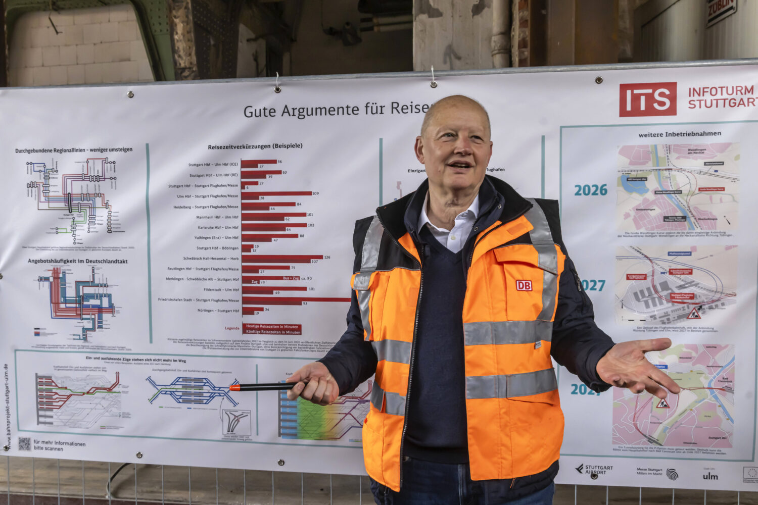 Eine Person in oranger Weste vor einem Plakat mit Diagrammen und Text.