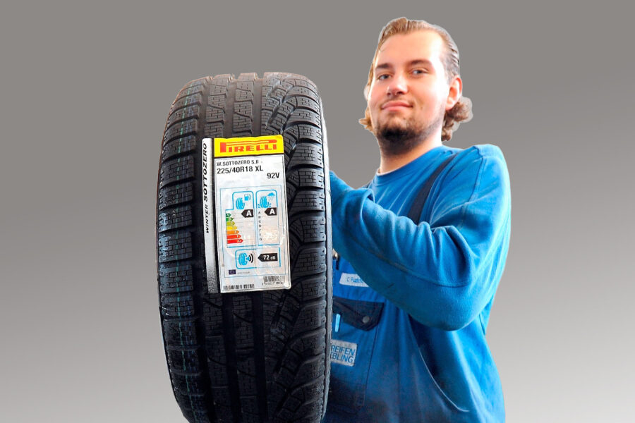 Person hält Autoreifen mit Label, auf grauem Hintergrund.