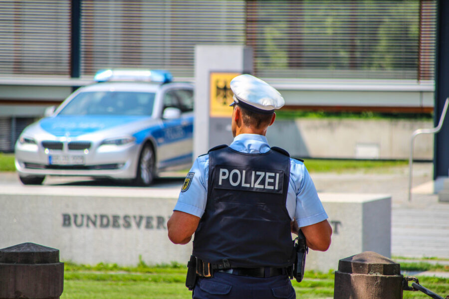Polizist von hinten, daneben ein Polizeiauto, Schriftzug "BUNDESVER" sichtbar.